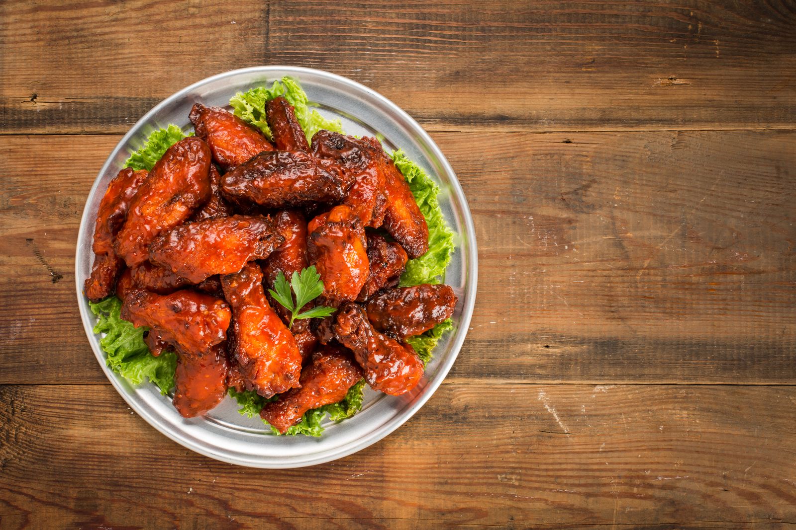 Sticky glazed barbecue chicken wings coated in dark red sauce on a metal plate over a rustic wooden table