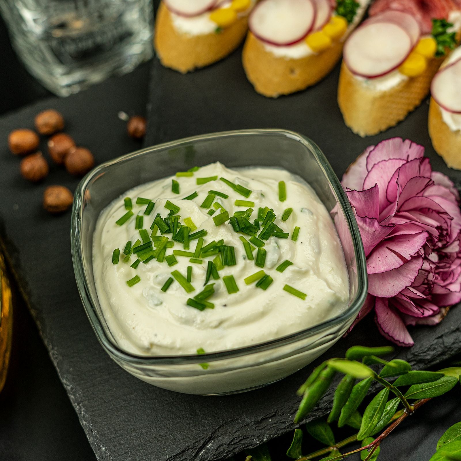Creamy white buttermilk ranch dip topped with freshly chopped chives in a glass bowl on a black slate board